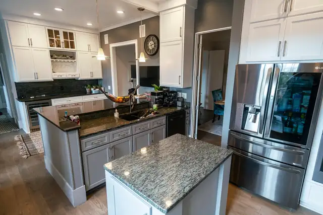Kitchen with gray and white Shaker cabinets, a granite-topped island, glass-front upper cabinets and stainless appliances