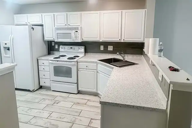 White kitchen with granite-look counters, a corner sink and new tile floor