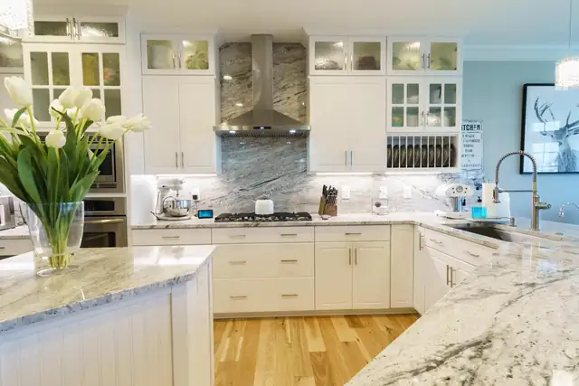 White cottage-style kitchen with a granite island, glass pendants and stainless appliances