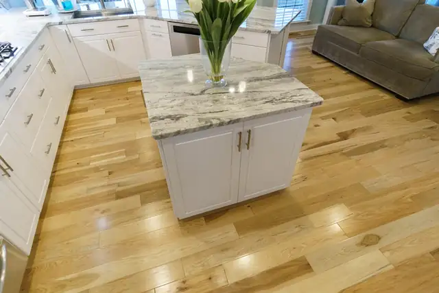 White cottage-style kitchen island with a gray granite top and brushed nickel pulls on oak floors