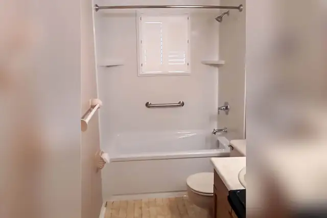 New white acrylic bathtub and wall surround with a grab bar, replacing an old green tub