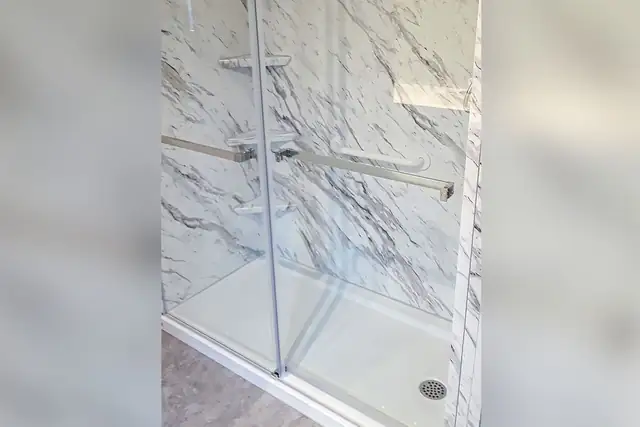 Walk-in shower with marble-look acrylic walls and a frameless glass door after a tub removal