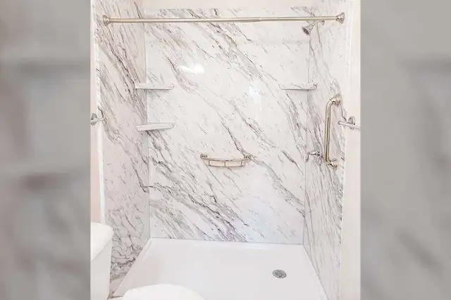 Tub to shower conversion with Calcutta stone-look acrylic walls, a low-threshold pan and chrome grab bar