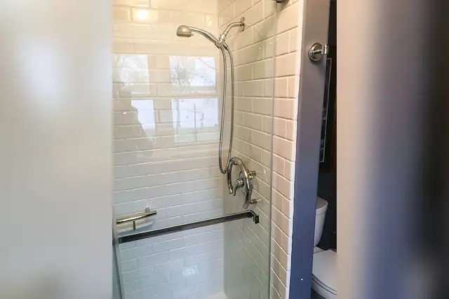 Replacement shower with subway tile-look acrylic walls, a glass door and black grab bar